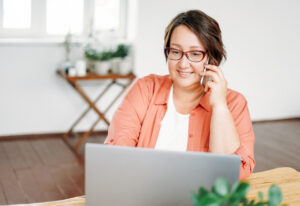 Adult charming brunette woman in glasses plus size body positive working with laptop at the home Plans